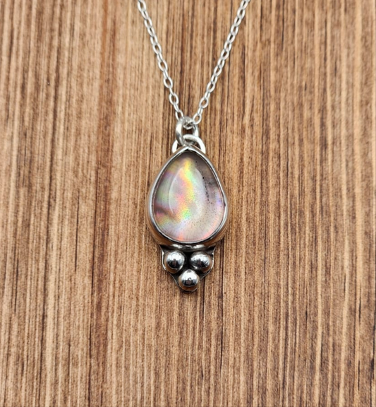 Silver necklace with a teardrop-shaped pendant on a wooden surface