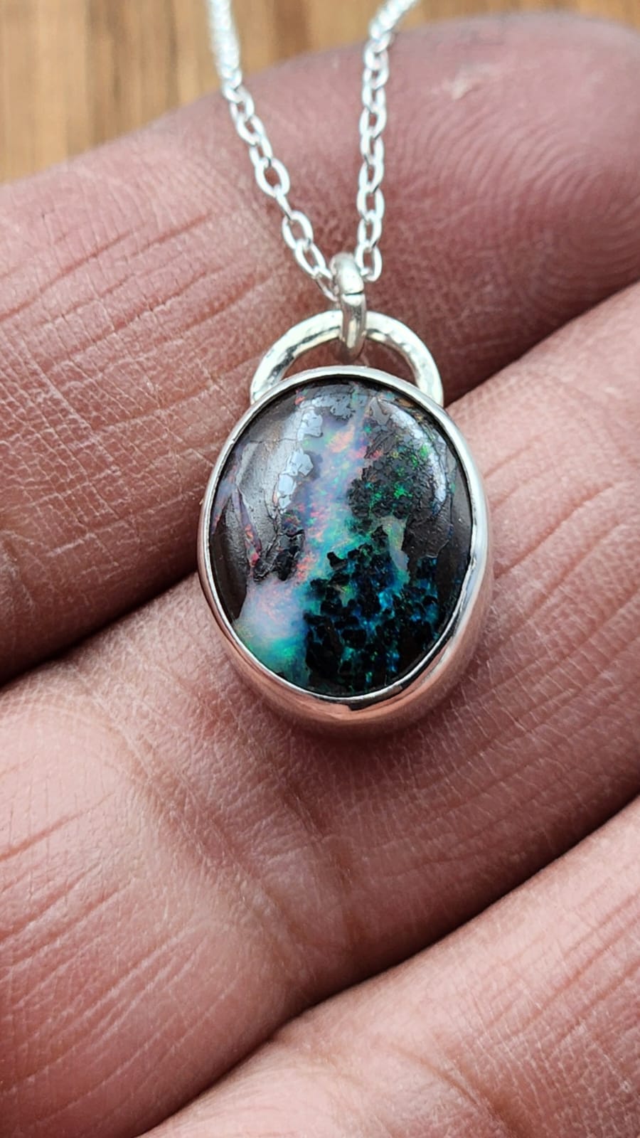 Necklace with a pendant featuring a multicolored stone held between fingers.