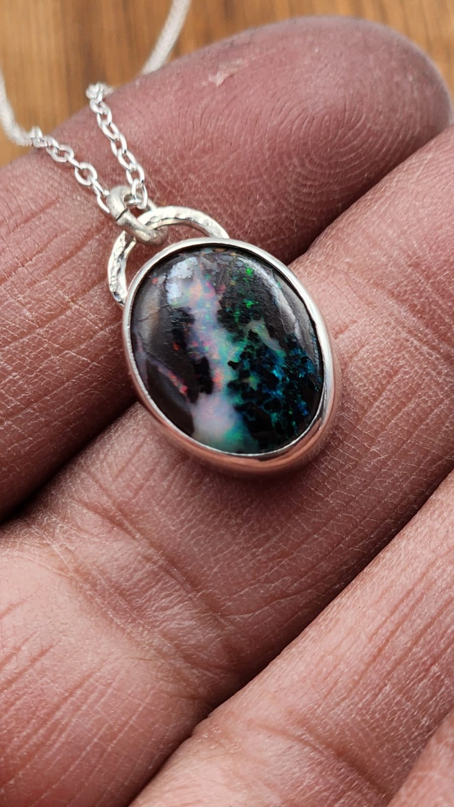 Silver necklace with a pendant featuring a colorful stone held in a hand.
