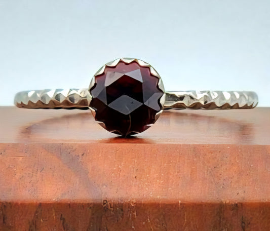 Silver ring with a red gemstone on a wooden surface
