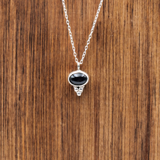 Silver necklace with a black pendant on a wooden surface
