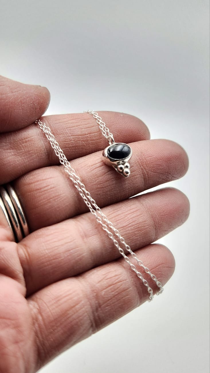 Silver necklace with a black pendant held between fingers on a light background