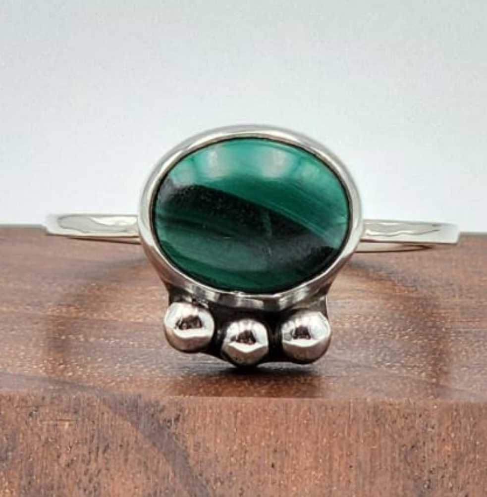 Silver ring with a green stone on a wooden surface