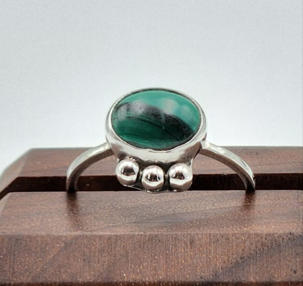 Silver ring with a green gemstone on a wooden stand