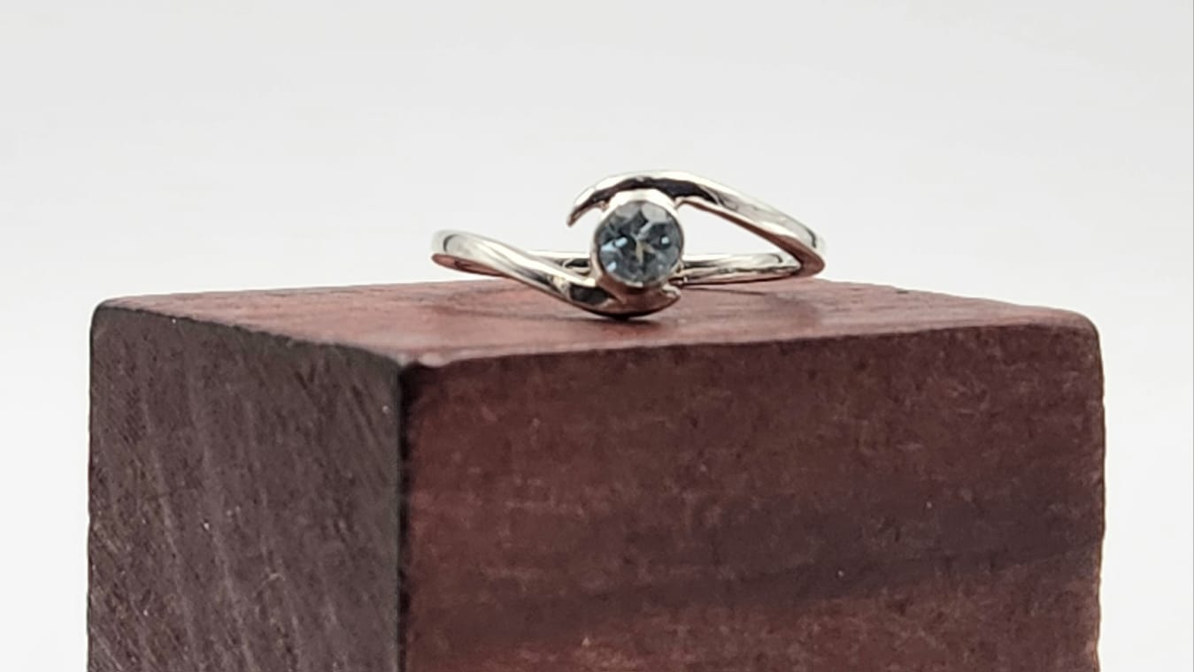 Sterling Silver Bypass ring set with a faceted Santa Maria Aquamarine gemstone on a wooden block.