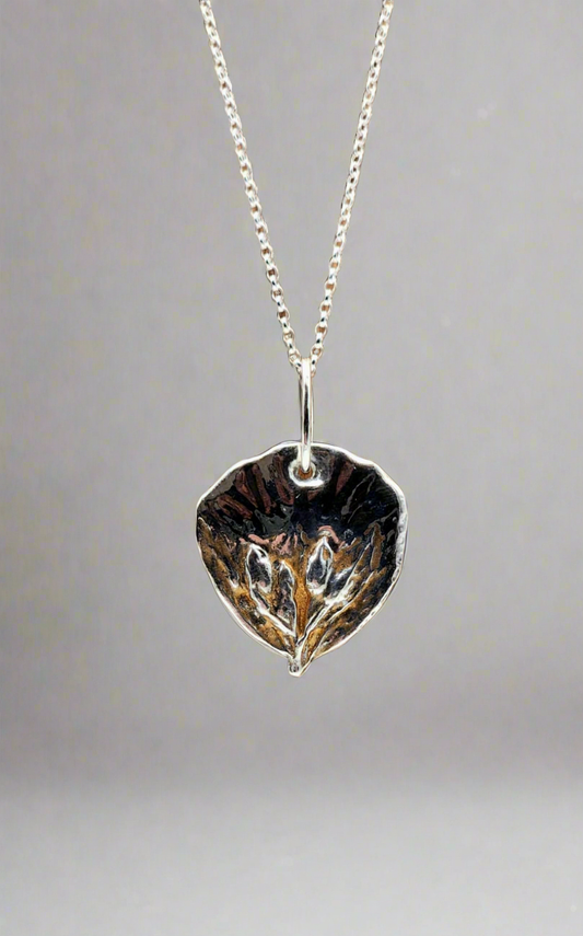 Silver leaf-shaped pendant on a chain against a gray background