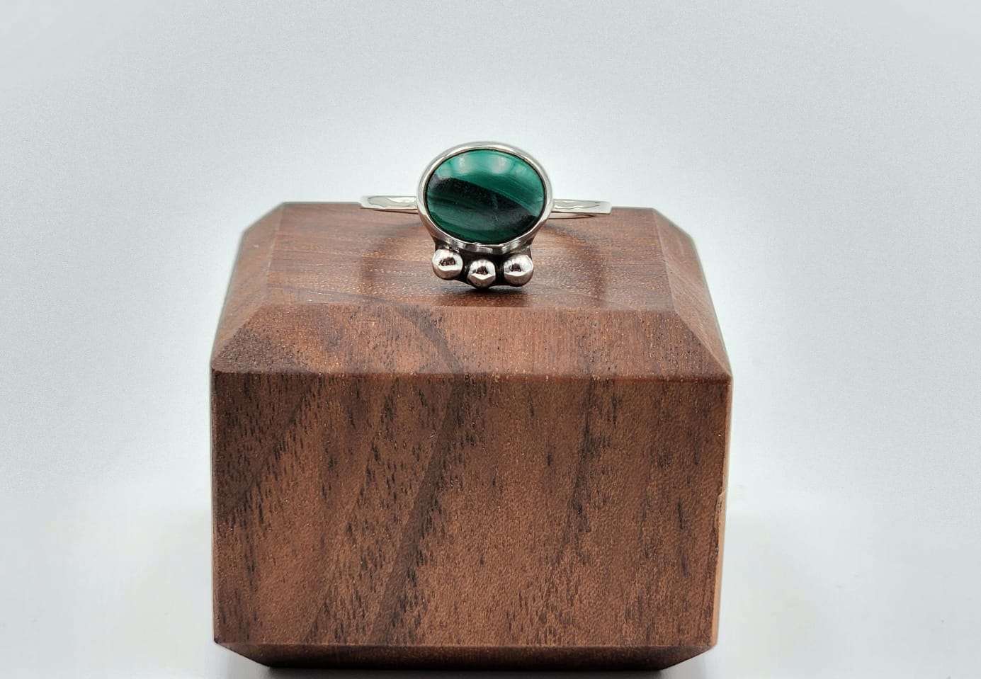 Silver ring with a green gemstone on a wooden block against a white background
