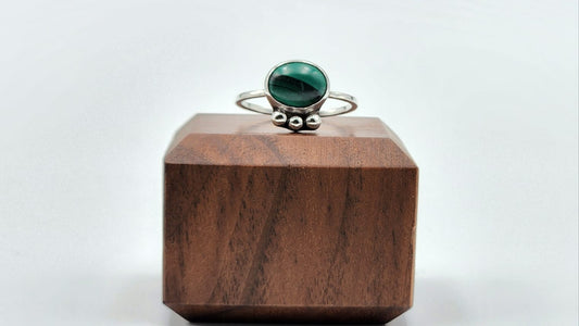 Silver ring with a green gemstone on a wooden block against a white background