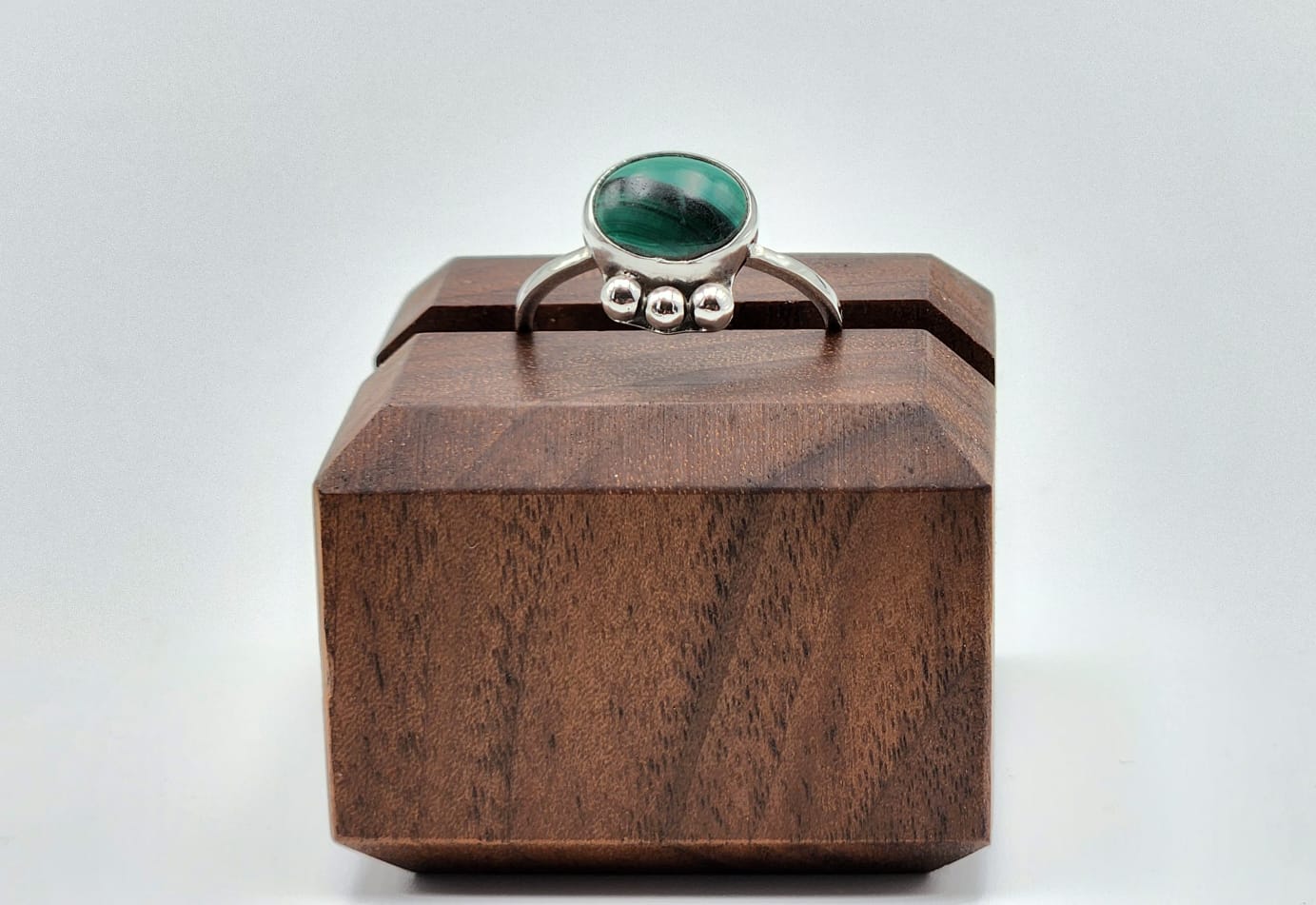 Silver ring with a green gemstone on a wooden box against a white background
