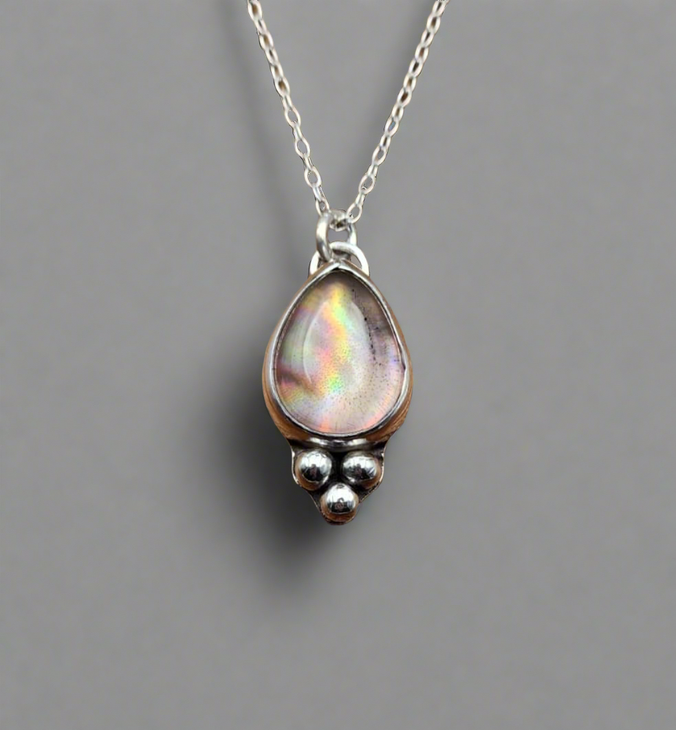 Teardrop-shaped pendant with rainbow iridescent stone on a chain against a gray background