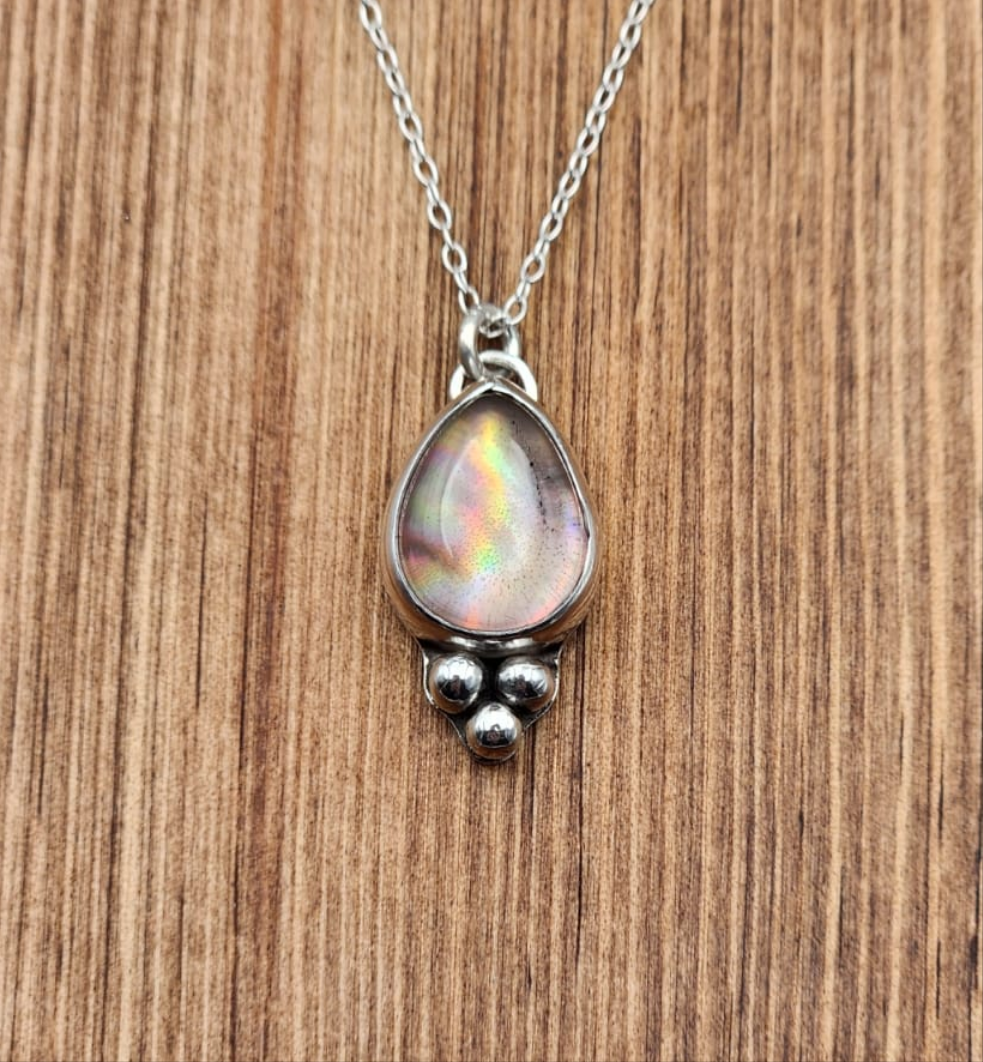 Silver necklace with a teardrop-shaped pendant on a wooden surface