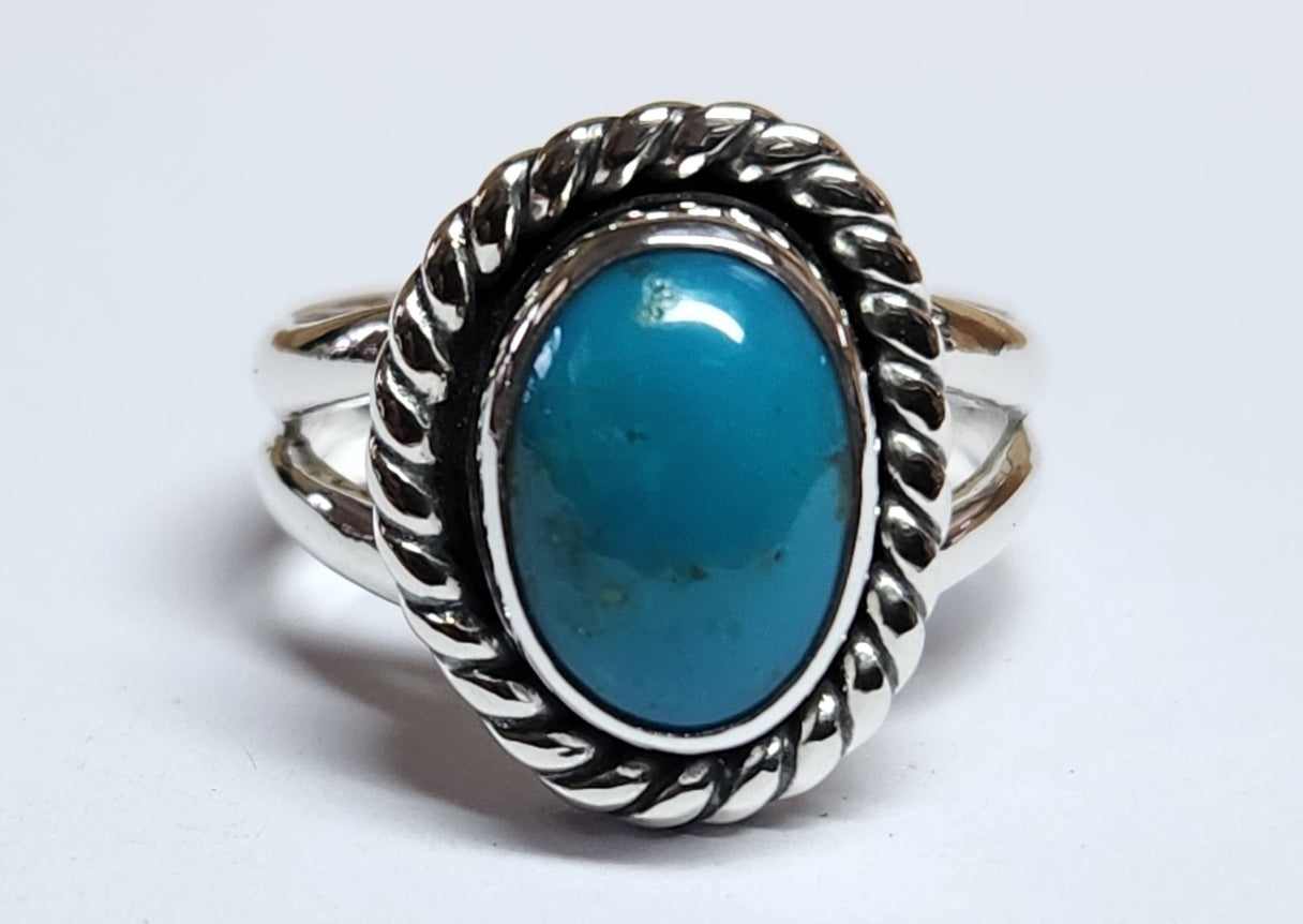 A sterling silver ring featuring an oval turquoise cabochon stone in a decorative twisted rope bezel setting, shown on a plain light gray background.