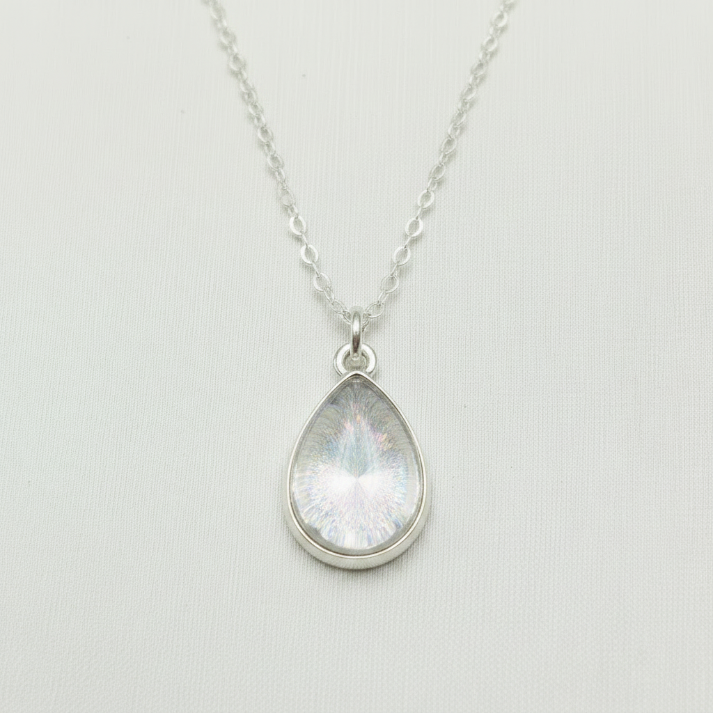 A silver teardrop pendant necklace featuring an iridescent stone with a white vertical band, suspended from a delicate silver chain against a light gray textured background