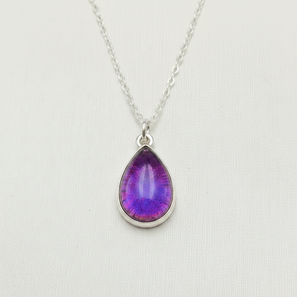 A silver teardrop pendant necklace featuring a textured amber-orange resin center, displayed on a clean white textured background.