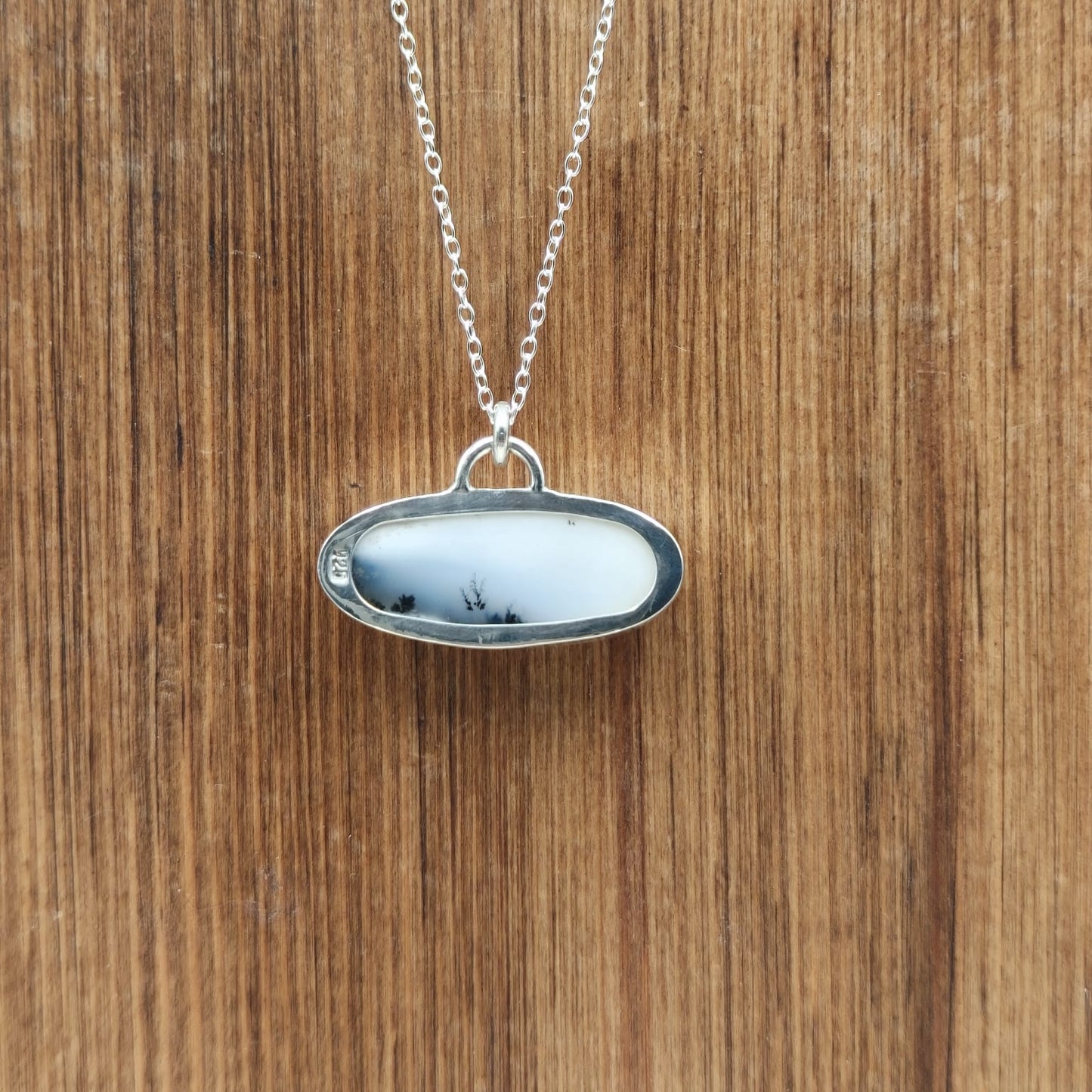 Silver necklace with an oval pendant on a wooden surface