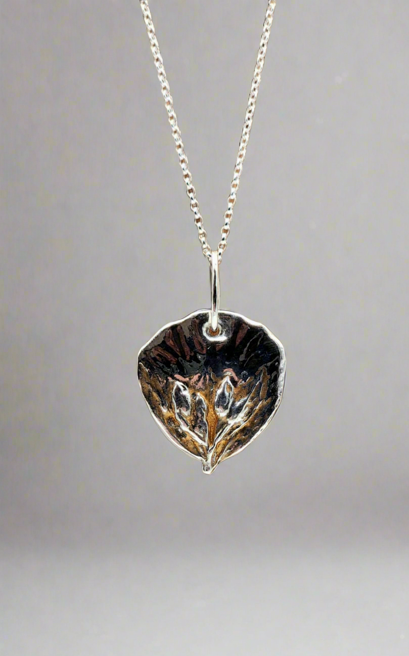 Silver leaf-shaped pendant on a chain against a gray background