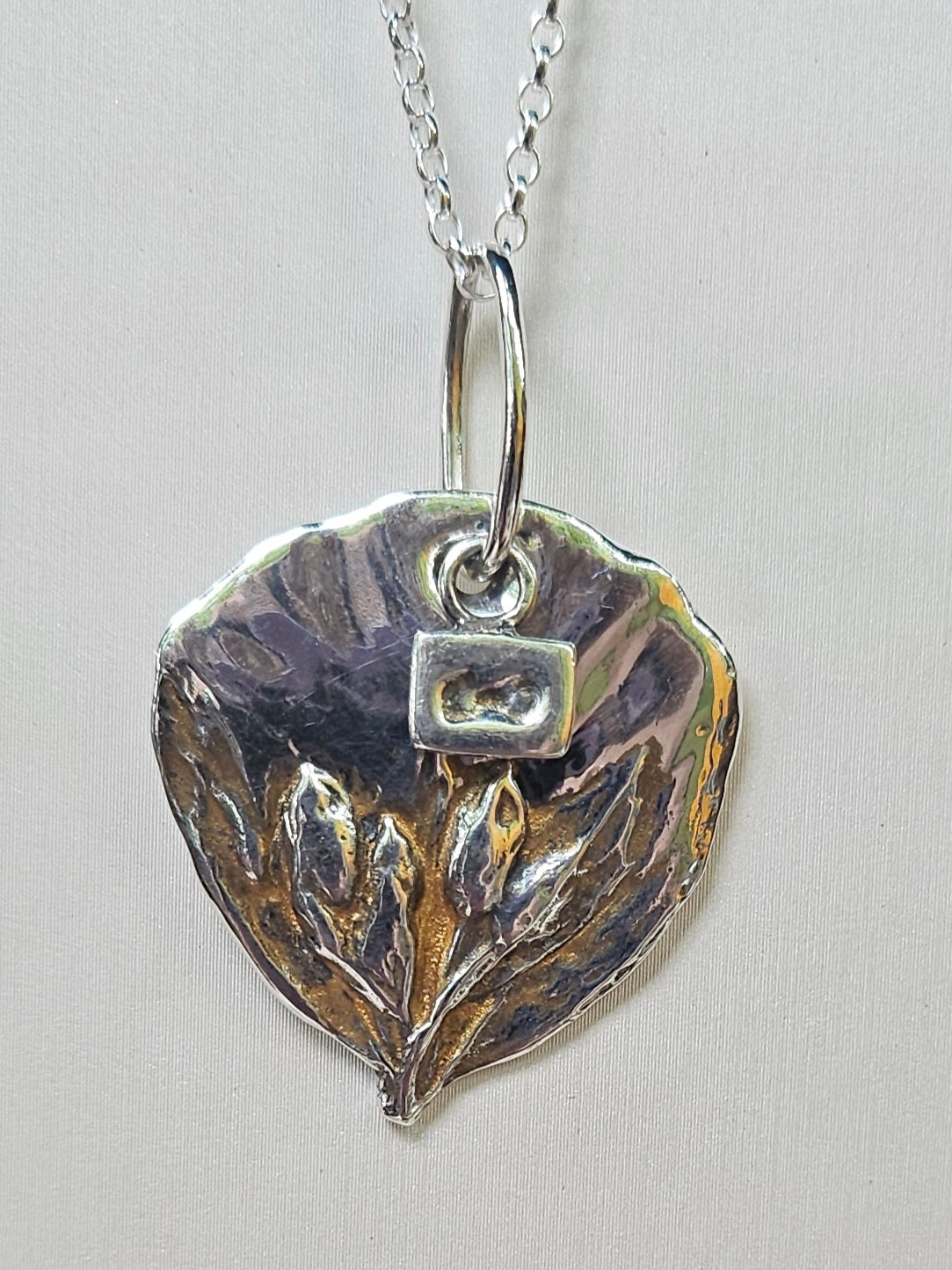 Silver pendant with flower design on a chain against a light gray background