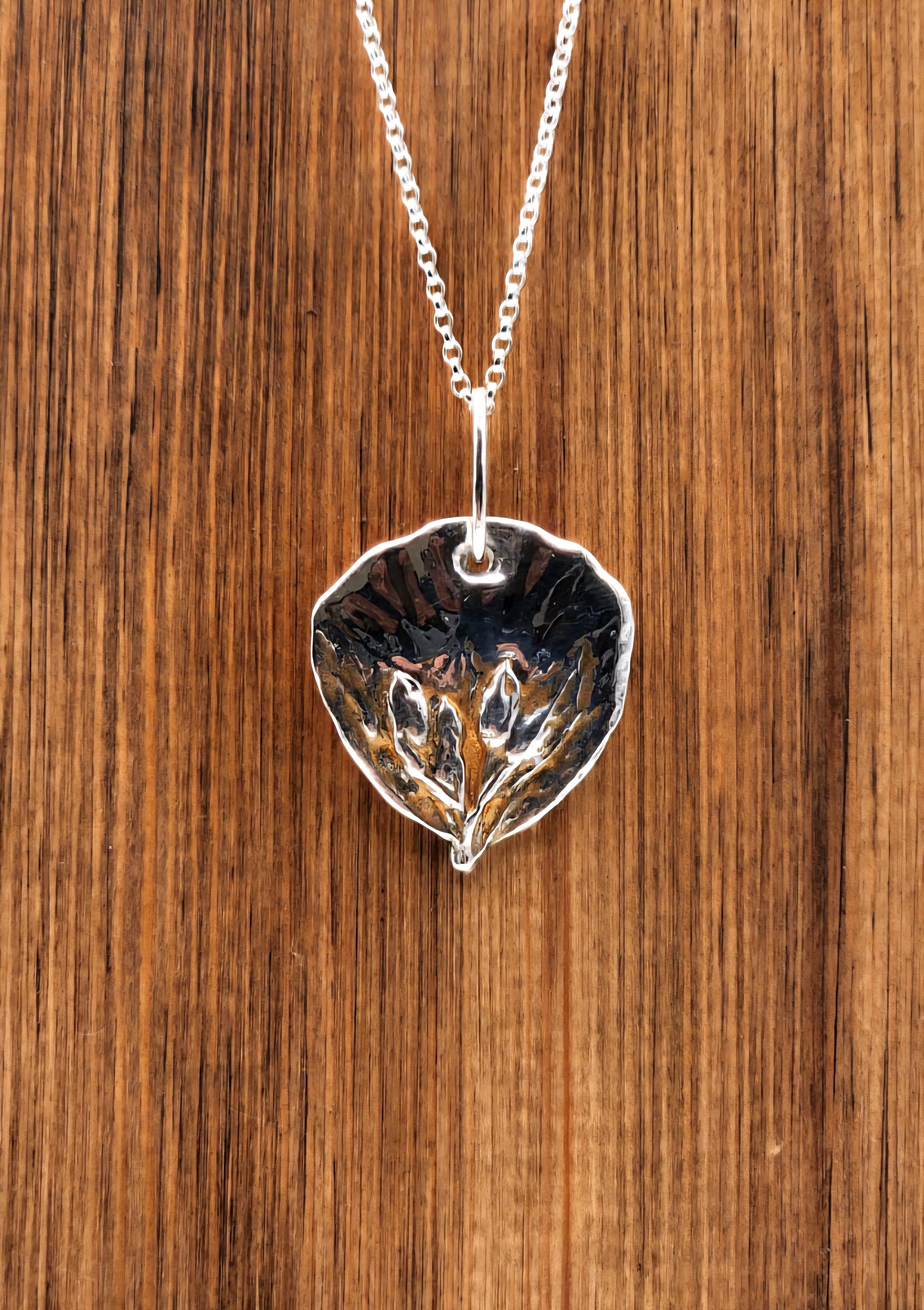 Silver leaf-shaped pendant necklace on a wooden surface