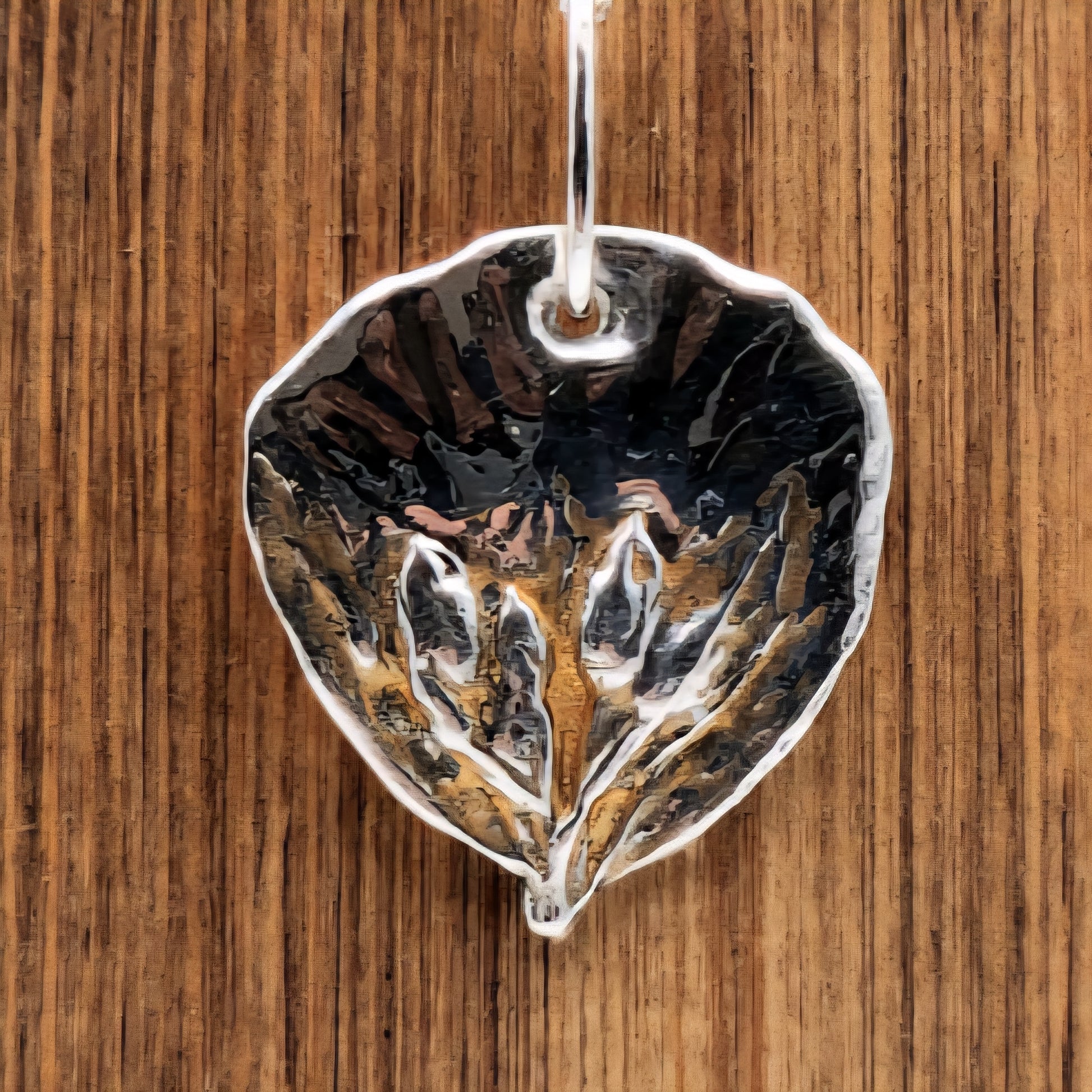 Silver pendant with leaf design on a wooden background