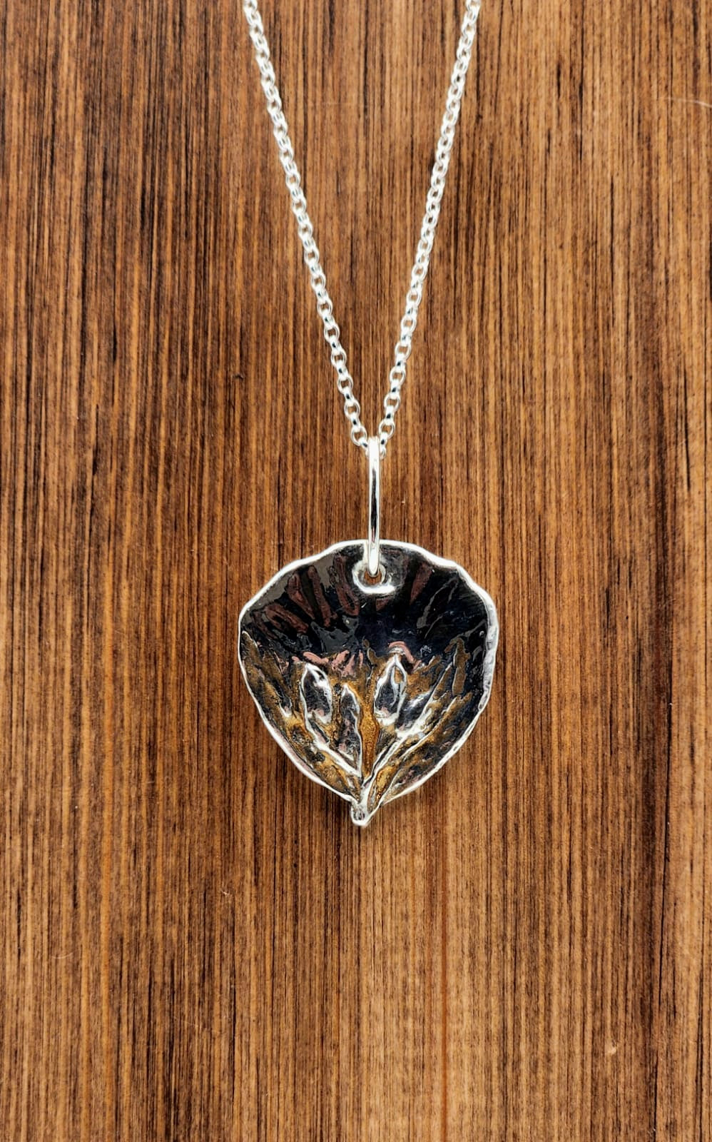 Silver leaf-shaped pendant necklace on a wooden surface