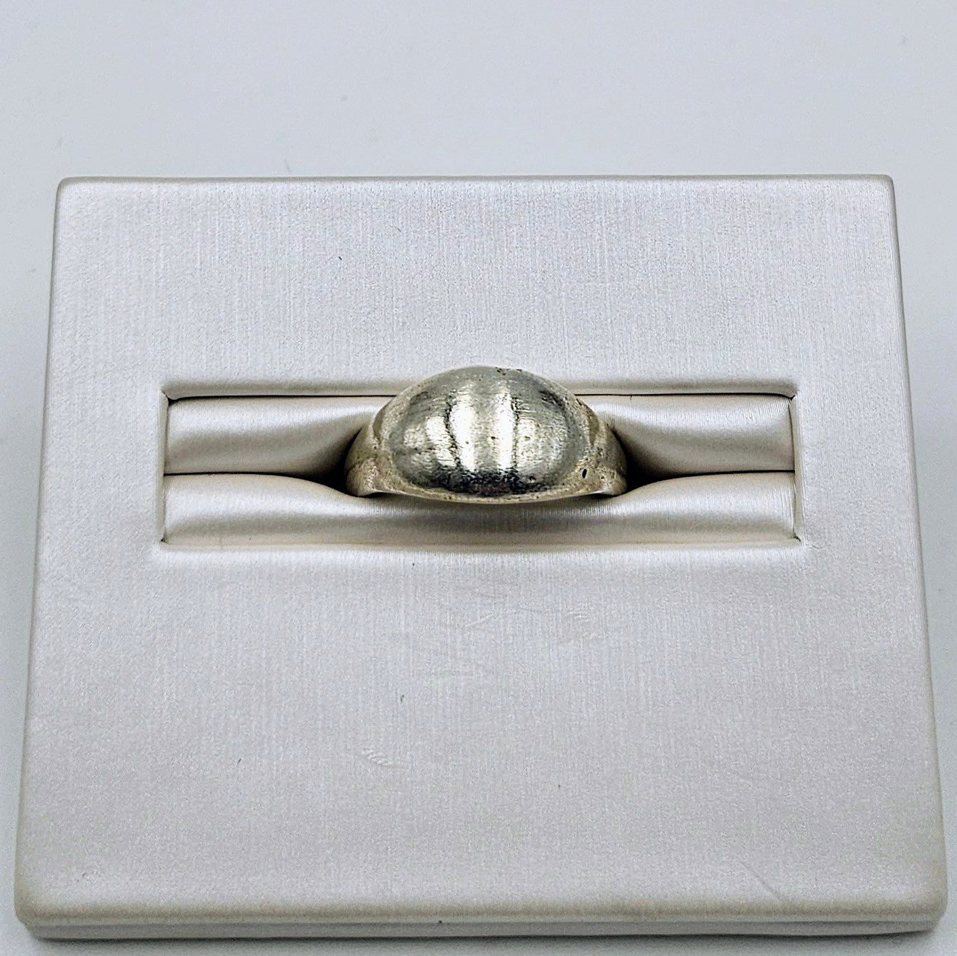 A silver ring with a textured, ribbed dome-shaped face, displayed in a white satin-lined presentation box.