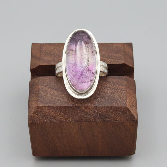 Ring with a purple stone on a wooden stand and grey background