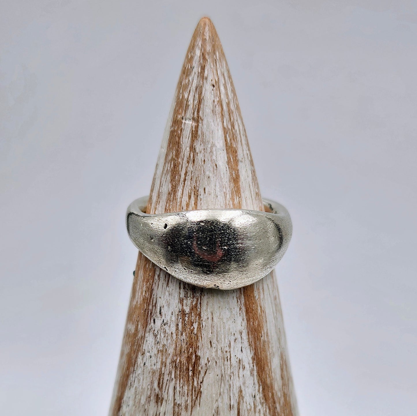 A textured silver ring displayed on a pointed wooden cone stand against a light gray background.