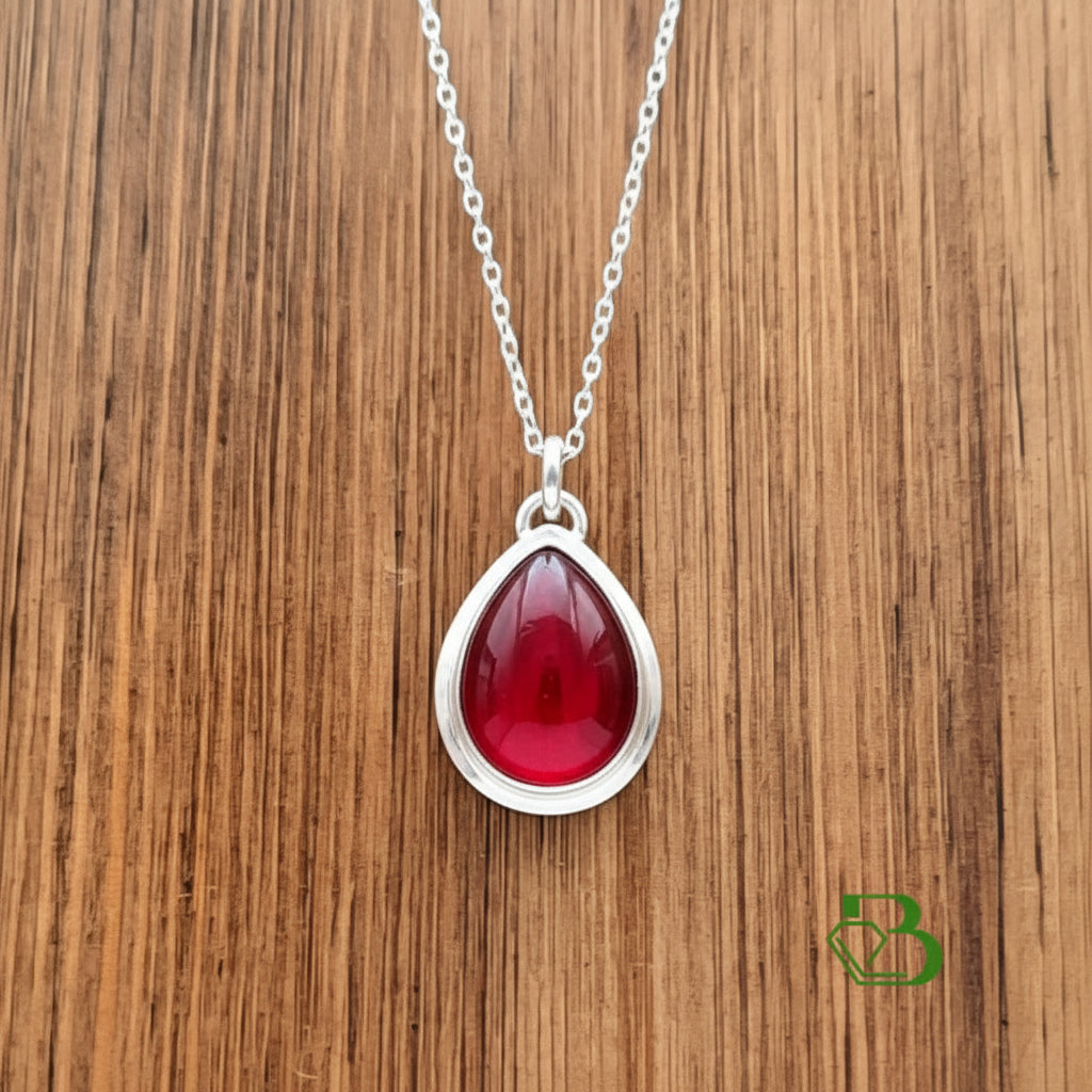 A silver teardrop pendant  displayed on a brown wooden surface.