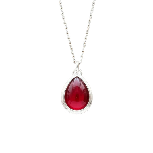 A silver teardrop pendant  displayed on a brown wooden surface.